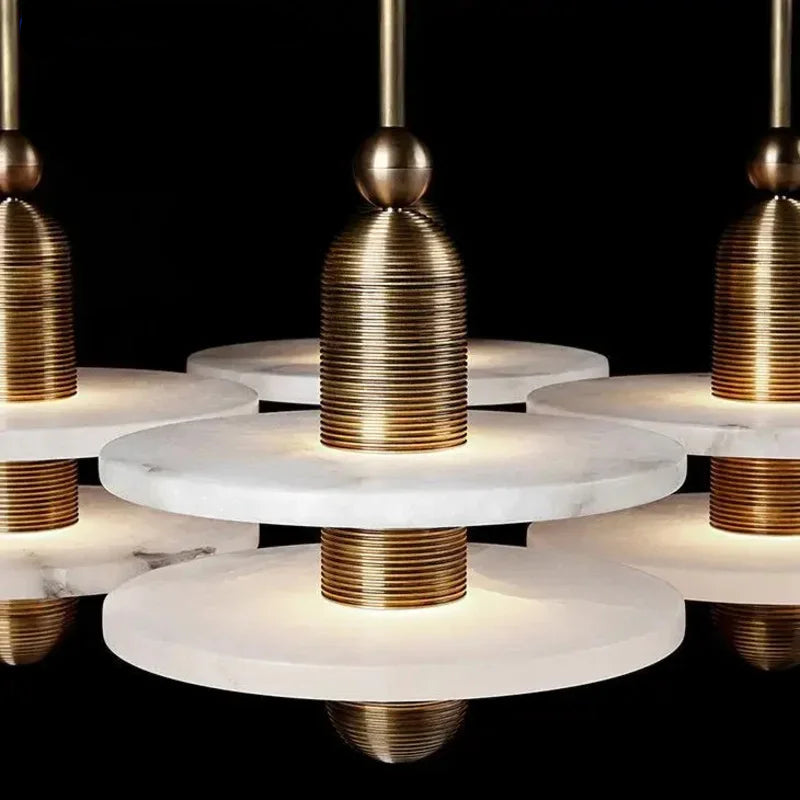 Modern chandelier pendant light with layered white marble discs and ribbed brass metal accents, shown against a black background.